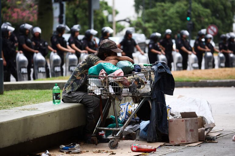 Un indigente descansa próximo a una hilera de policías antidisturbios que protegen el Ministerio de Capital Humano en Buenos Aires. 