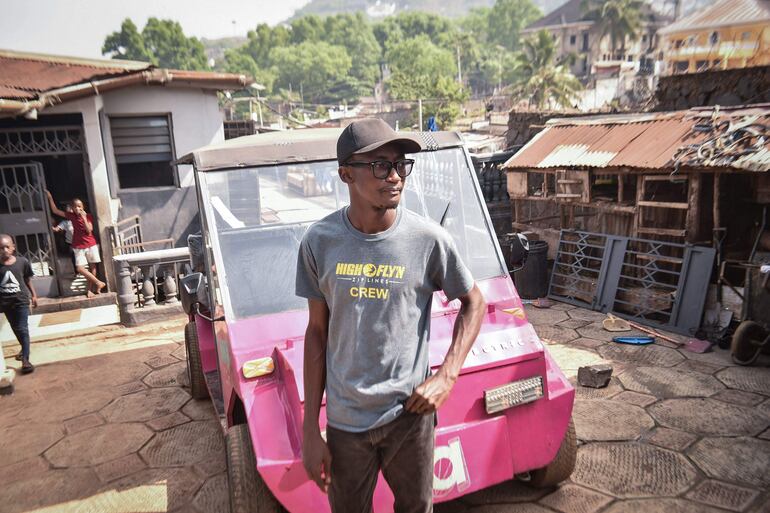 El innovador autodidacta James Samba posa frente a un vehículo eléctrico ecológico que fabricó con metales reciclados en Freetown.
