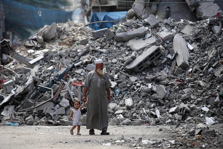 Un anciano sostiene a un niño de la mano mientras pasa junto a un edificio arrasado por un bombardeo israelí en el campo de refugiados de Bureij en el centro de la Franja de Gaza.