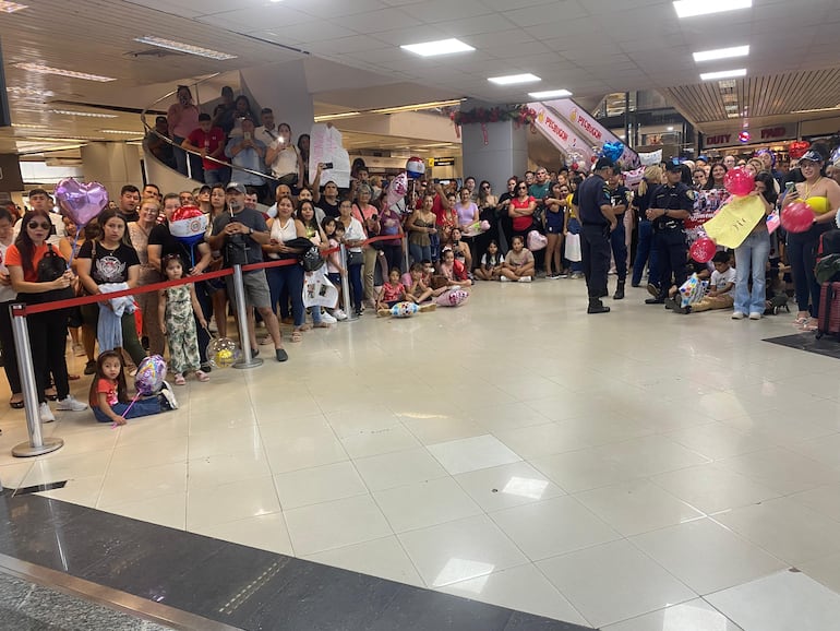 Una multitud de familiares y amigos esperando con entusiasmo y carteles de bienvenida en el aeropuerto, listos para recibir a sus seres queridos.