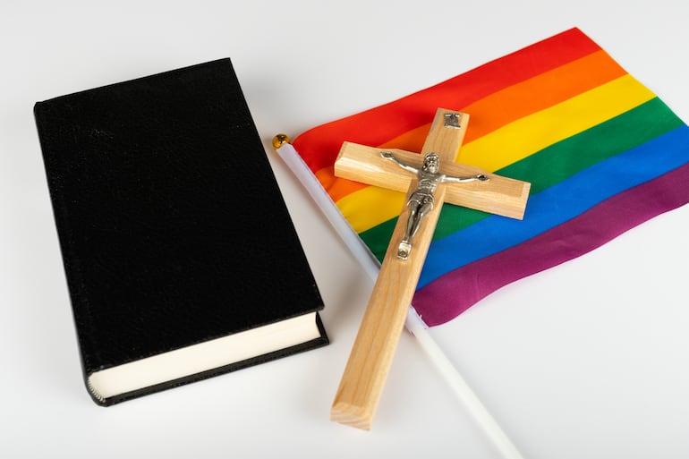 Una biblia, una cruz y una bandera del orgullo gay.