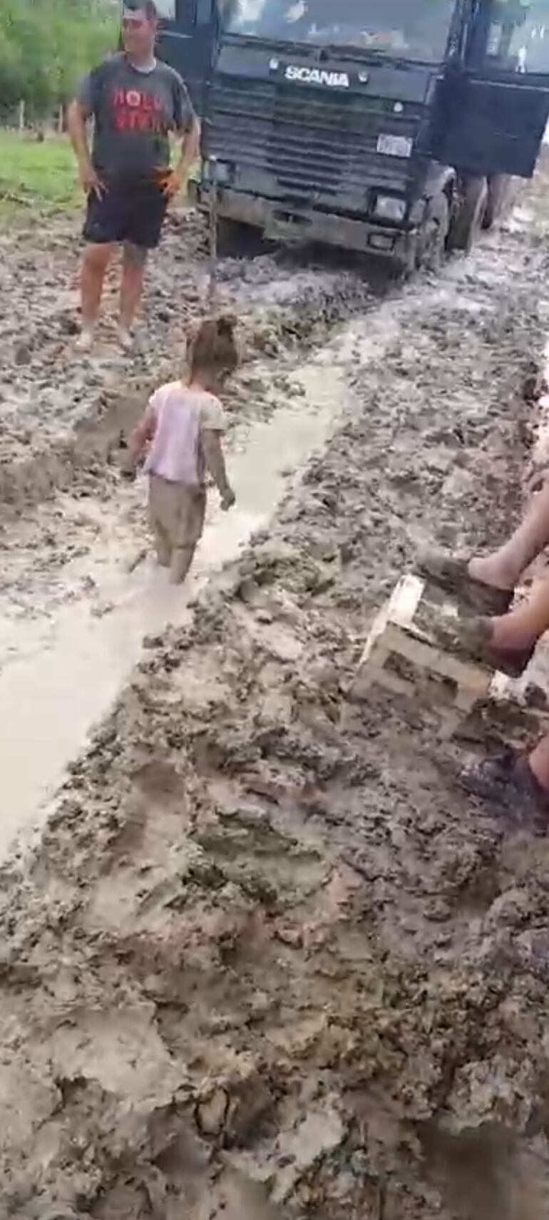 Una criatura juega en el barro ante la mirada de su padre, cuyo vehículo quedó atascado en el camino.