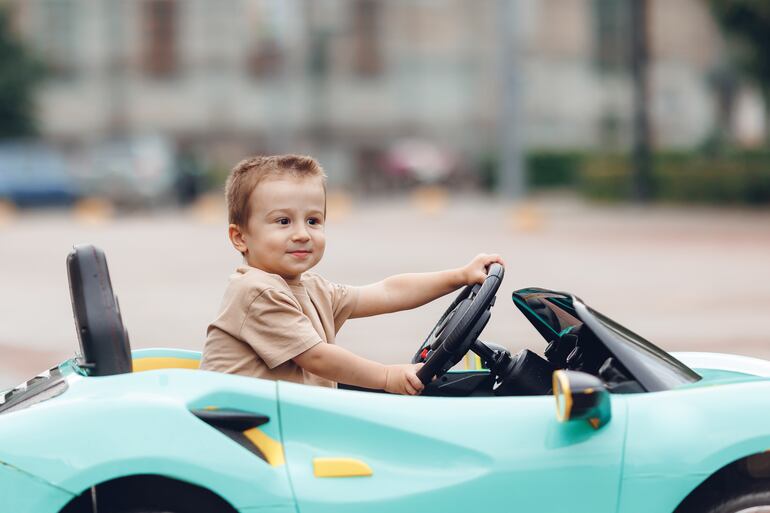 Un niño sonriente conduce un pequeño auto de juguete.