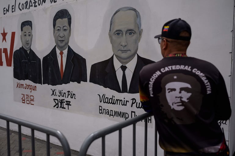 Un miembro de la organización civil "Catedral Combativa", que apoya al régime chavista, observa un mural en el que aparecen los presidentes Kim Jong-Un, de Corea del Norte (i);  Vladimir Putin, de Rusia (C) y Xi Jinping, de China (d), en Caracas. 