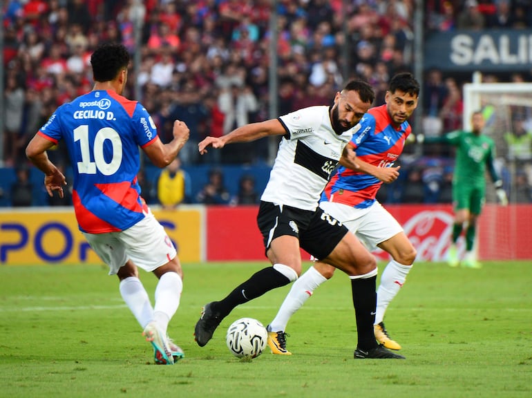 Ramon Martínez (c), futbolista de Olimpia, disputa el balón ante la marca de Cecilio Domínguez (i) y Federico Carrizo (d), jugadores de Cerro Porteño, durante un partido del fútbol paraguayo en el estadio La Nueva Olla, en Asunción.
