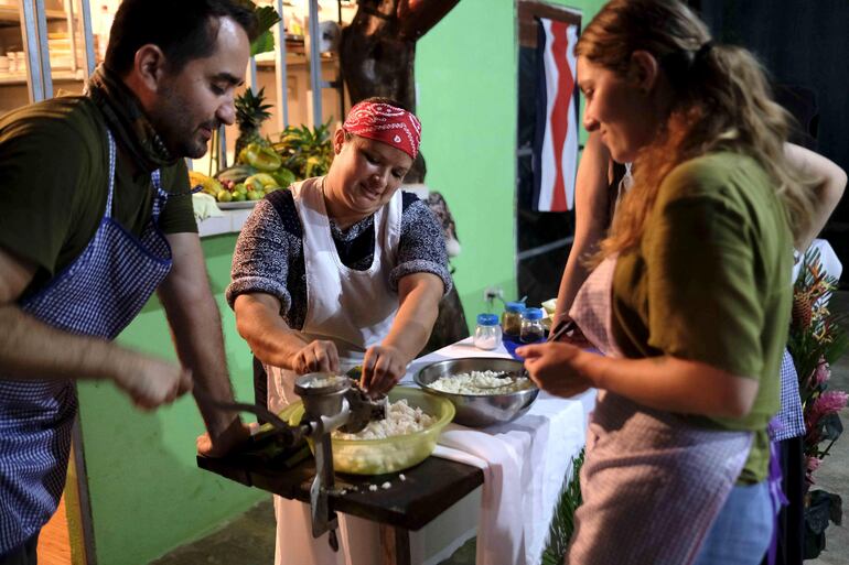 Varios turistas participan de unas clases de cocina tradicional, impartidas por una mujer miembro de la Asociación Agroecológica Juanilama, la cual se dedica al turismo rural comunitario y está conformada en su mayoría por mujeres amas de casa.