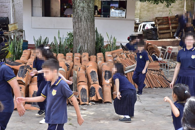 Las tejas están puestas sobre el cordón de cemento de un frondoso árbol de mango donde los estudiantes corretean.