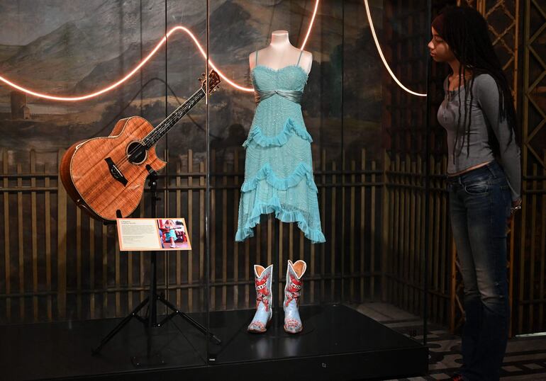 Una visitante de galería observa el conjunto usado por la artista estadounidense Taylor Swift en su gira Soul2Soul II, con el vestido diseñado por BCBG Max Azria y las botas de vaquero de Liberty Boot Co. 