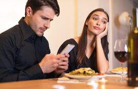 Un hombre revisa su teléfono celular durante una cena y no presta atención a su pareja.