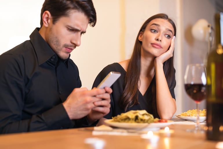 Un hombre revisa su teléfono celular durante una cena y no presta atención a su pareja.