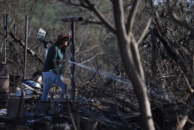 Una residente, que no dio su nombre, usa una manguera de jardín para apagar los puntos calientes en la casa de un vecino que fue destruida por un incendio forestal el 12 de agosto de 2023 en Kula, Hawaii. 