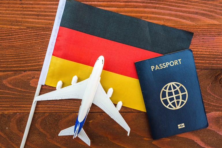 Imagen ilustrativa: una bandera de Alemania con un pequeño avión y un pasaporte.