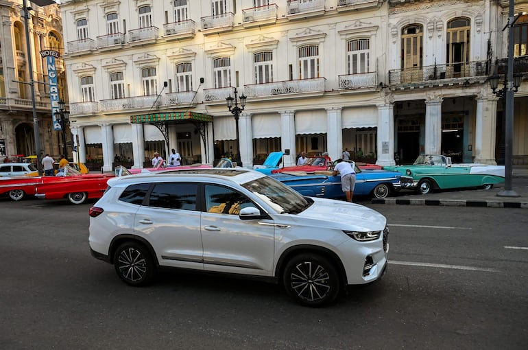 Un automóvil moderno circula por una calle frente a viejos automóviles estadounidenses en La Habana.  