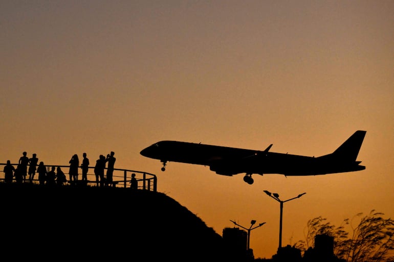 La gente observa un avión aterrizando al atardecer cerca del Aeropuerto Internacional Jorge Newbery en Buenos Aires.