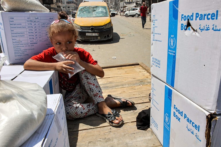 Una niña con una bolsa de agua sentada junto a paquetes de ayuda humanitaria de la ONU, el pasado martes en la Ciudad de Gaza.