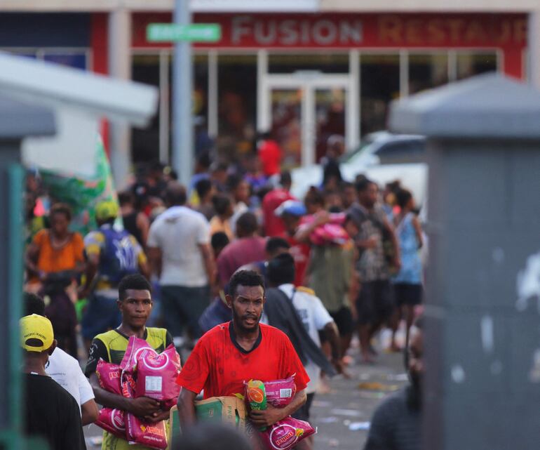 La gente lleva artículos mientras las multitudes abandonan las tiendas con bienes saqueados en medio de un estado de disturbios en Port Moresby el 10 de enero de 2024.