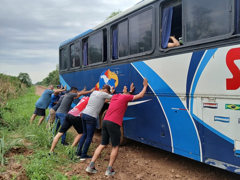 Los pasajeros en medio del barro tratando de impedir que el colectivo caiga a la cuneta.