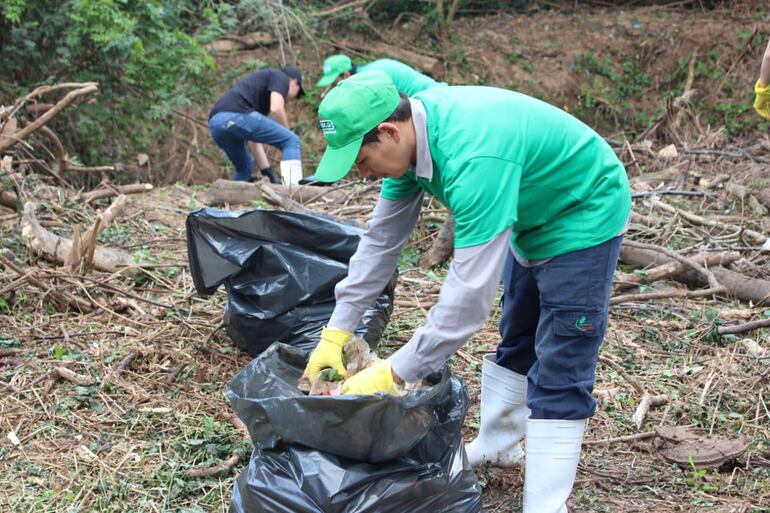 hombre con remera verde, pantalón azul y una bota depositando basura en una bolsa negra. Foto: Gentileza