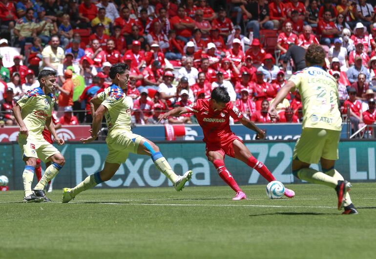 Robert Morales, delantero paraguayo del Toluca, consigue sacar el disparo hacía la portería del América pese a la presencia de tres jugadores del equipo rival.