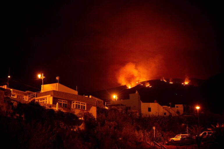 Una fotografía tomada en la noche del 19 de agosto de 2023 muestra los frentes del incendio forestal en las colinas sobre las casas, en el valle de Guimar en la isla canaria de Tenerife. El incendio, que según las autoridades es el "incendio más complejo" que ha afectado a las Islas Canarias en 40 años, estalló el 15 de agosto en una zona montañosa del noreste de Tenerife. 