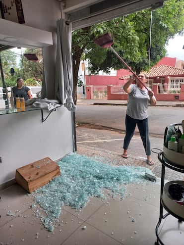 Las trabajadoras del local tratan de juntar los vidrios rotos en el salón de belleza. Un solitario ladrón rompió el blíndex con su cuerpo.