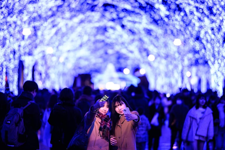 Dos mujeres se toman "selfies" en una zona iluminada con luces navideñas en el distrito de Shibuya, en Tokio, Japón.