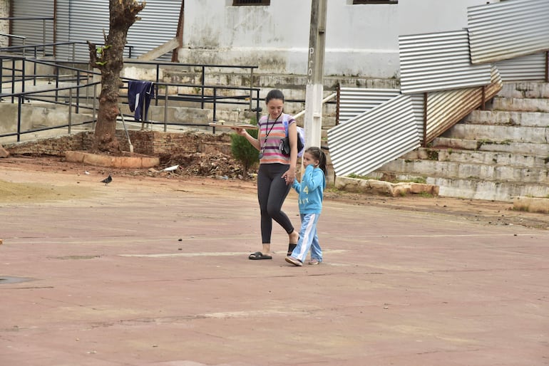 Una mamá ayuda con la bandeja a su pequeña hija, luego de cruzar todo el patio, donde también se construye un salón de clases en la escuela Pedro Escalada, Lambaré.