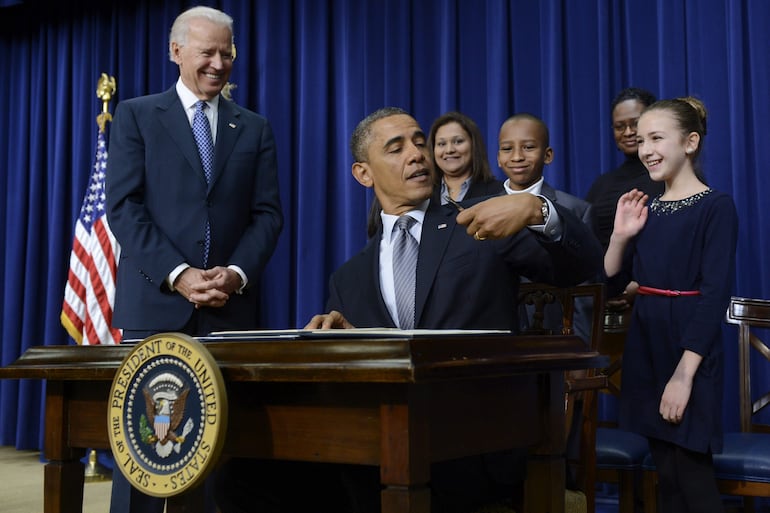 El entonces presidente estadounidense Barack Obama (c) bromea con una niña por el hecho de ser zurdo mientras firma 23 órdenes ejecutivas para endurecer el control de armas junto al vicepresidente Joe Biden (i) en Washington, Estados Unidos, en una foto de archivo fechada el 16 de enero de 2013.