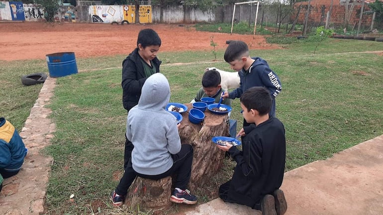 Estudiantes comen poroto con arroz sobre un tronco en una escuela de Capiatá. No tienen comedor.