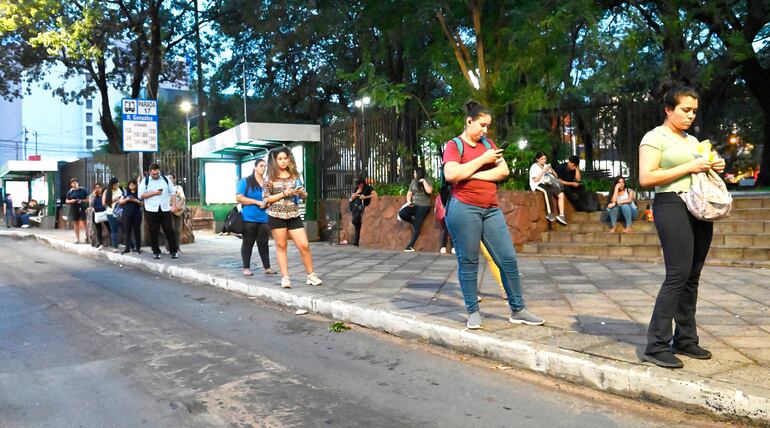 Pasajeros apostados   en una parada sobre la avenida Mariscal López, frente a la plaza Infante Rivarola del barrio Villa Morra, observan sus celulares para sobrellevar la larga espera.