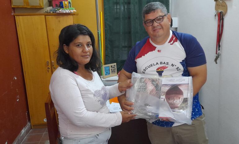 Joel Peña, director de la escuela básica N° 92 San Miguel, hace entrega del kit escolar a una madre, cuyo hijo cursara el 7º grado en la institución.