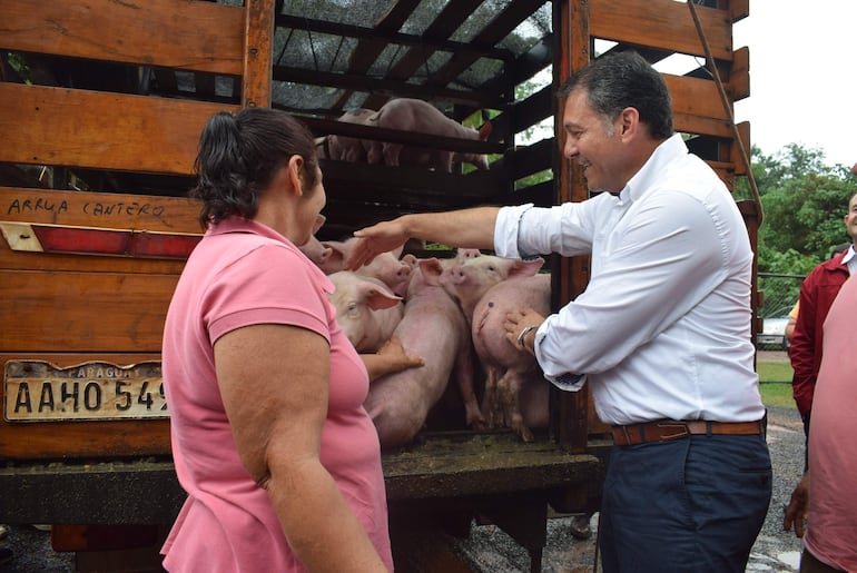 El ministro del MAG, Carlos Giménez, muestra a la presidenta del Comité, Martina Saldívar uno de los ejemplares de cerdo que recibirá su organización.