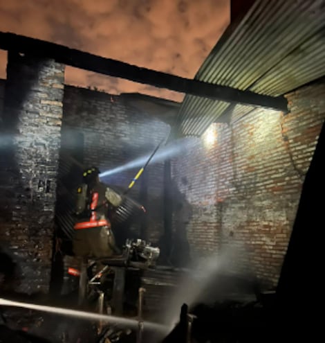 Bomberos trabajan en el enfriamiento del local comercial consumido por el fuego en Luque.