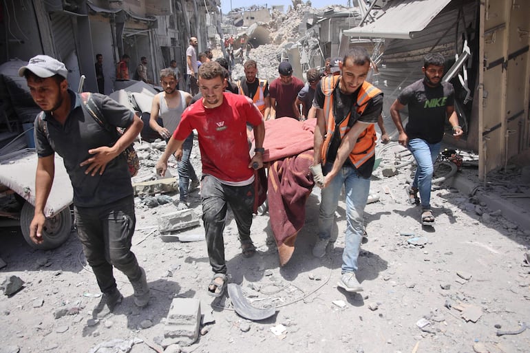 Varias personas trasladan un cuerpo rescatado de entre los escombros de un edificio destruido por un bombardeo israelí en la Ciudad de Gaza.