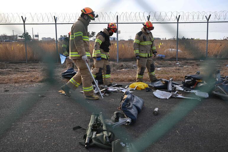 Restos del avión de Jeju Air un Boeing 737-800 son inspeccionados por bomberos en el aeropuerto internacional de Muan.