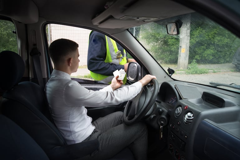 Un conductor entrega sus documentos y billetes a un policía. (Foto ilustrativa).