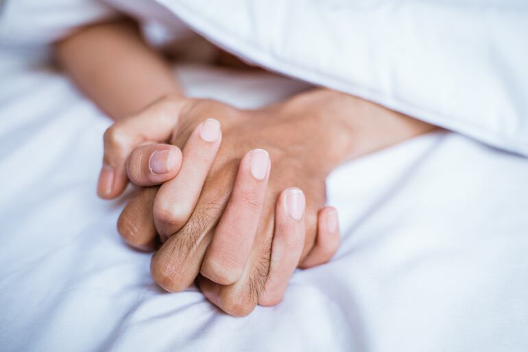 Una pareja se toma de la mano en la cama.