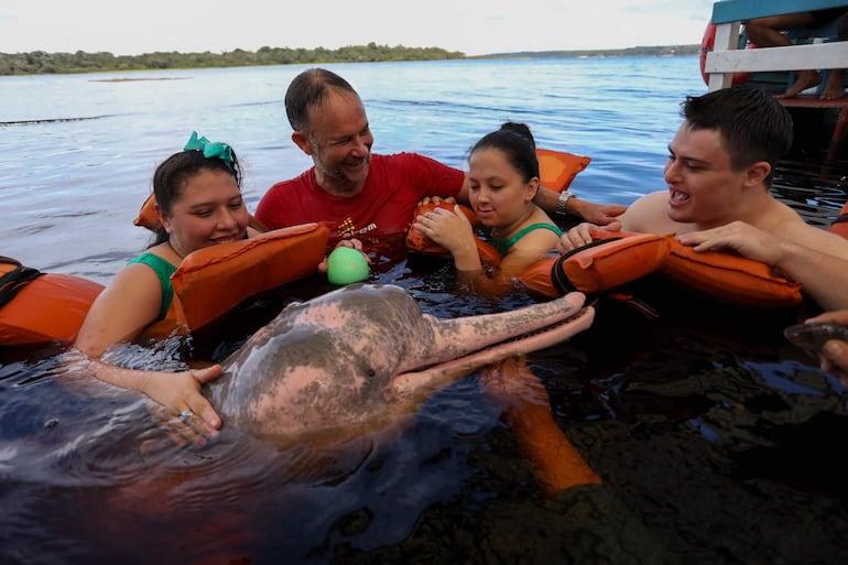 El fisioterapeuta Igor Simoes Andrade y jóvenes con discapacidades nadan con delfines rosados (Inia geoffrensis) en el río Negro en Iranduba, Brasil.