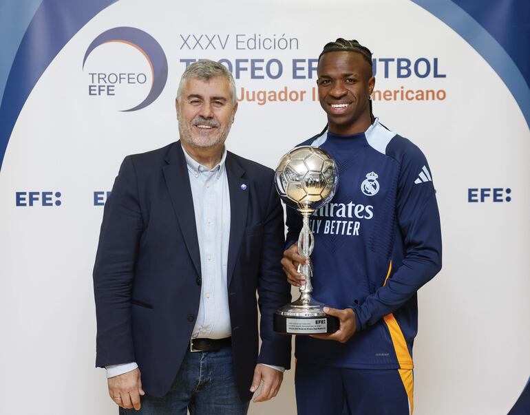 MADRID, 31/12/2024.- El delantero brasileño del Real Madrid Vinicius jr. (d), acompañado por el presidente de la Agencia EFE, Miguel Ángel Oliver (i), posa con el Trofeo EFE al Mejor Jugador Iberoamericano de Fútbol antes de participar en el entrenamiento realizado este martes, último día del año, en Valdebebas.Tras regresar el lunes al trabajo después del descanso navideño, el Real Madrid, que el viernes visita al Valencia en un partido pendiente de la duodécima jornada y que fue aplazado por la dana, se entrena este martes a puerta abierta, con acceso único para los socios del club. EFE
