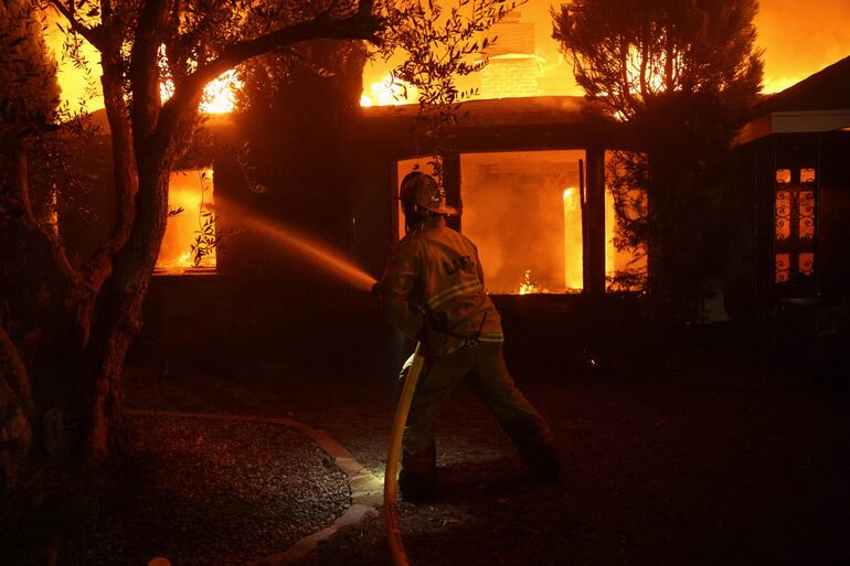 Un bombero apaga con mangueras una casa en llamas provocada por el incendio forestal de Palisades, en Pacific Palisades, Los Ángeles, California, EE.UU.