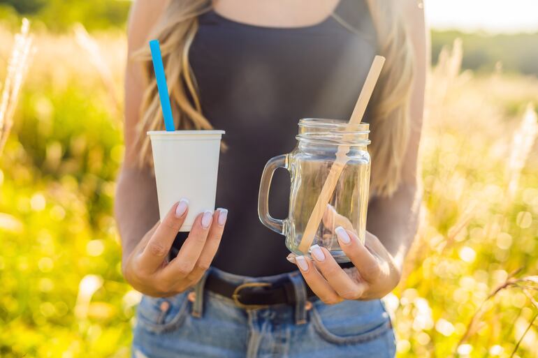 Una joven sostiene un vaso con una pajita de plástico y otro con una pajita de bambú.