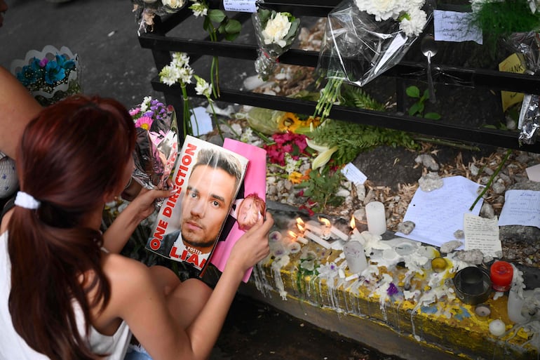 Una fanática sostiene una revista con una foto de Liam Payne, entre flores y velas.