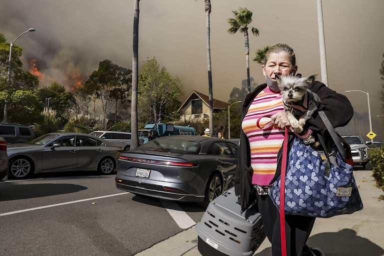 Una mujer lleva a un perro mientras evacúa un barrio amenazado por el incendio forestal de Palisades en Pacific Palisades, California, EE.UU., el 07 de enero de 2025.