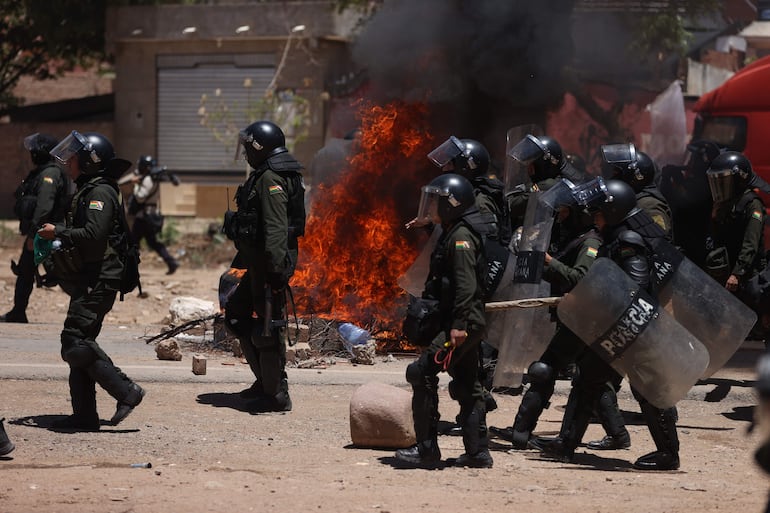 Integrantes de la Policía Boliviana caminan por una vía bloqueada y con llantas quemándose por simpatizantes del expresidente de Bolivia, Evo Morales (2006-2019), este viernes, en Parotani (Bolivia).