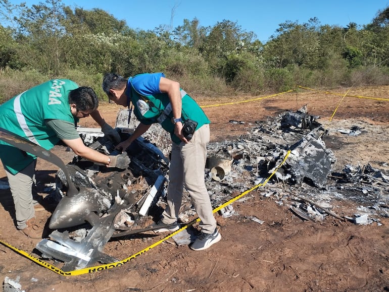 Funcionarios de Dinac revisan los restos del avión quemado en Tavaí.