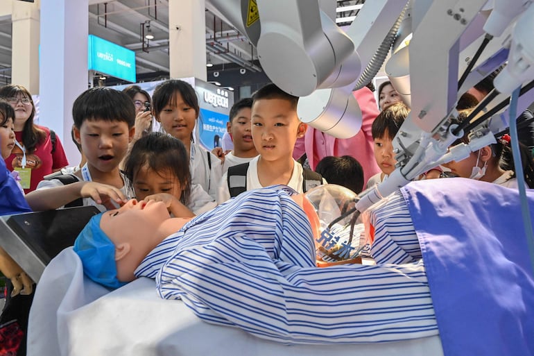 Alumnos observan a un robot que simula una operación a un paciente. 