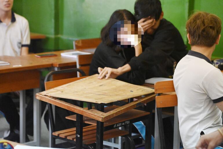 Estudiantes muestran una mesa pedagógica rota en una sala de clases del Colegio Nacional Asunción Escalada (CNAE).