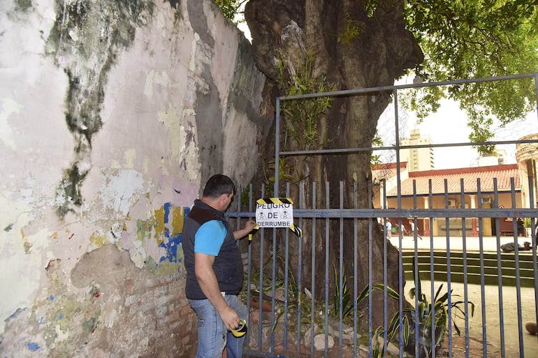 Personal de la escuela República Argentina coloca un cartel de advertencia cerca dela muralla que está en riesgo de derrumbe.