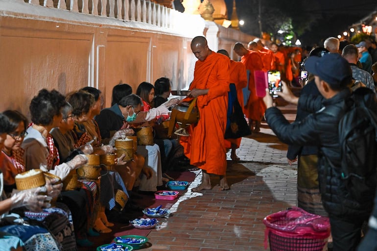 Los monjes budistas hacen fila al amanecer para recibir comida y limosnas de los devotos frente a una pagoda en Luang Prabang .