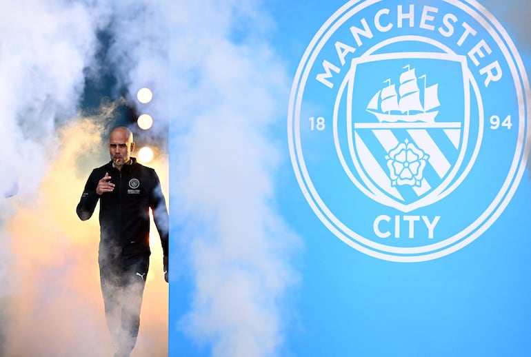 (FILES) Manchester City's Spanish manager Pep Guardiola smokes a cigar as he attends an event for fans with members of the Manchester City football team following an open-top bus parade through Manchester, north-west England on May 23, 2022, to celebrate winning the 2021-22 Premier League title. Pep Guardiola has extended his contract as Manchester City manager for a further two seasons, the Premier League champions announced on November 21, 2024.. (Photo by Oli SCARFF / AFP)